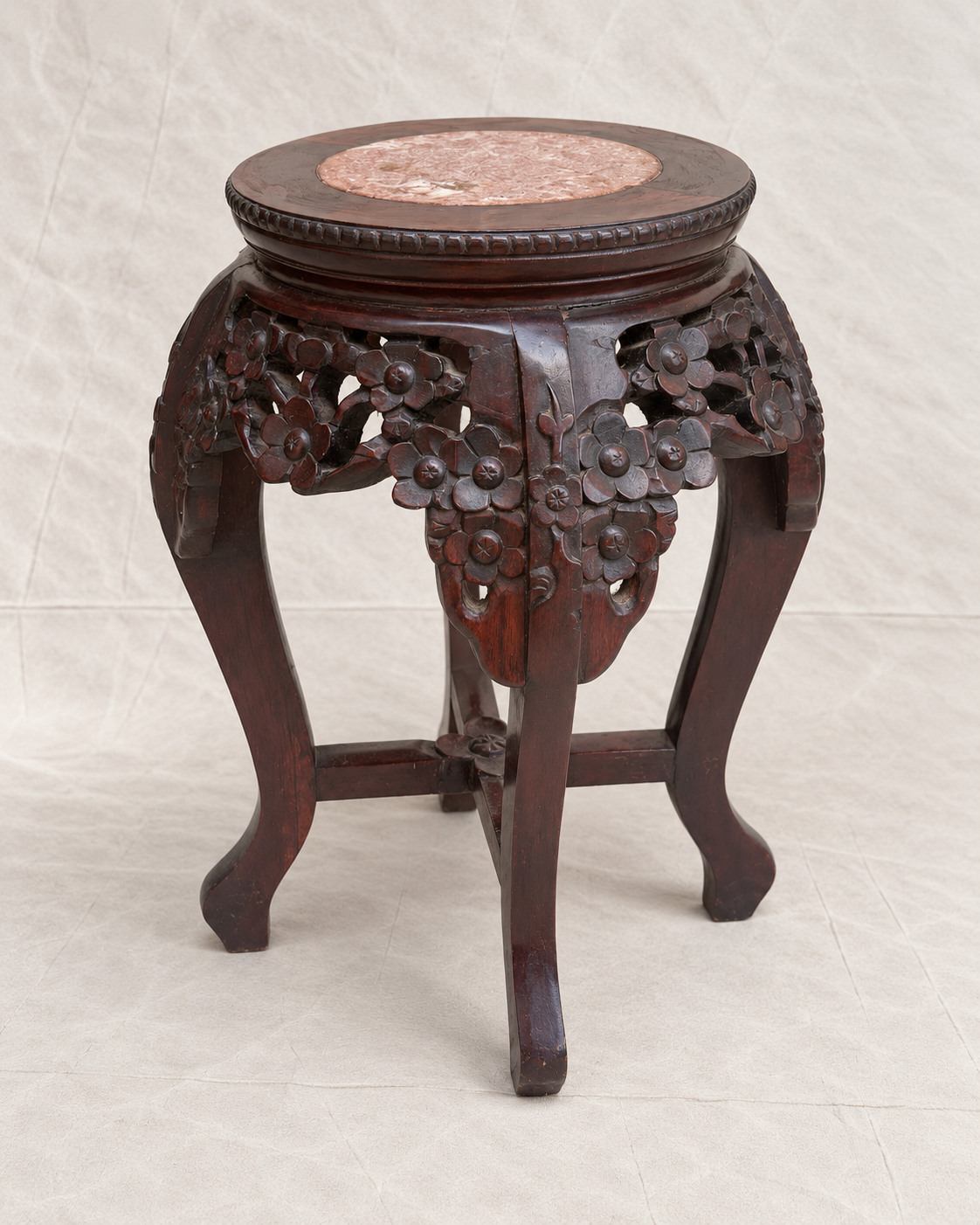 A dark carved wooden stool with floral details on the legs and a round pink stone inlay on the seat, photographed against a light fabric backdrop.