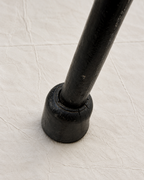 A close-up of a black metal leg or support post with a round base, resting on a textured off-white fabric surface.
