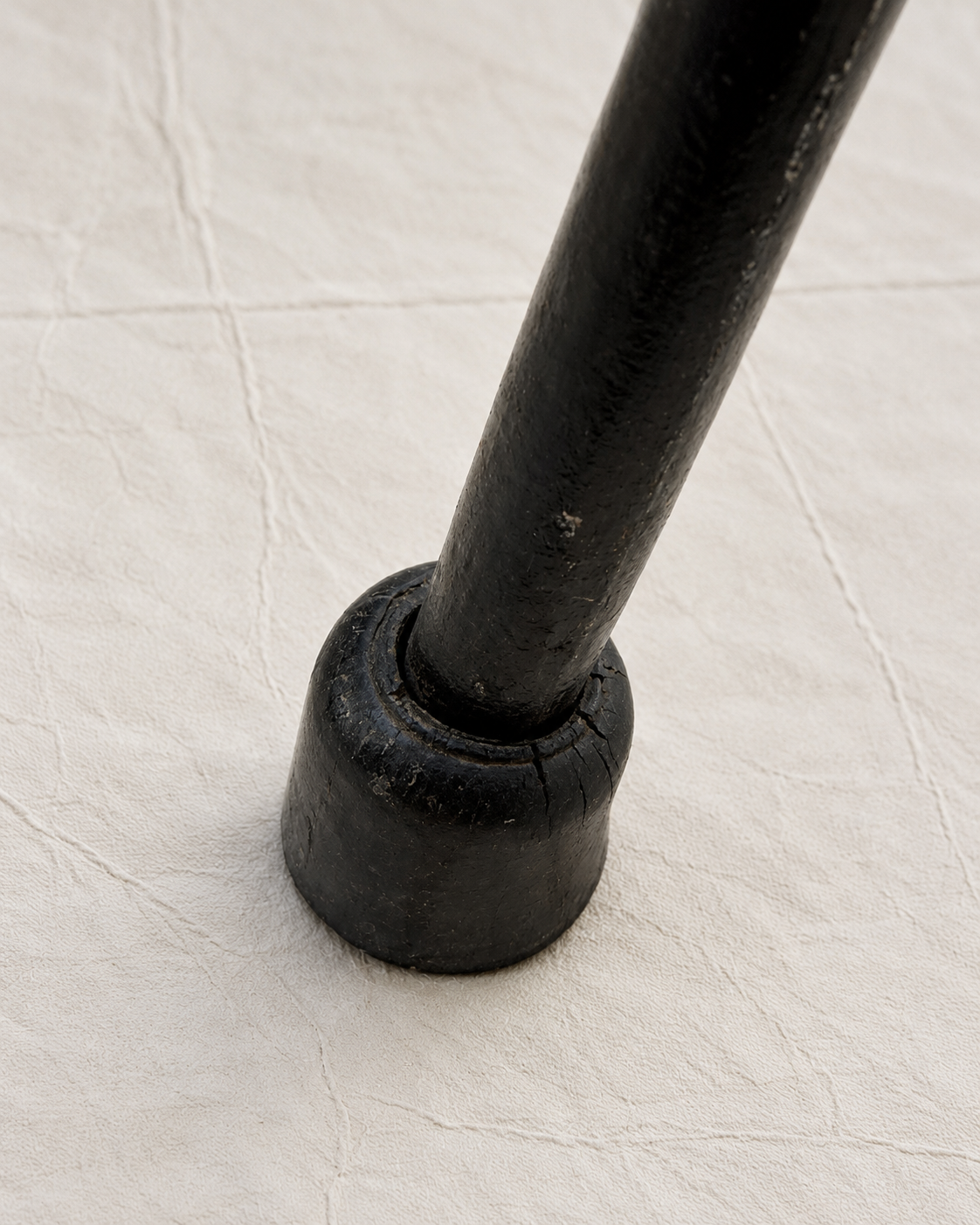 A close-up of a black metal leg or support post with a round base, resting on a textured off-white fabric surface.
