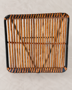 A square woven rattan or wicker chair seat/back panel with a black frame, photographed from above on a light neutral background.