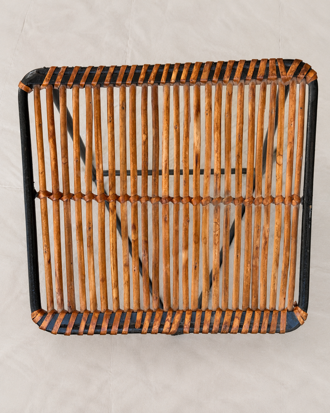 A square woven rattan or wicker chair seat/back panel with a black frame, photographed from above on a light neutral background.