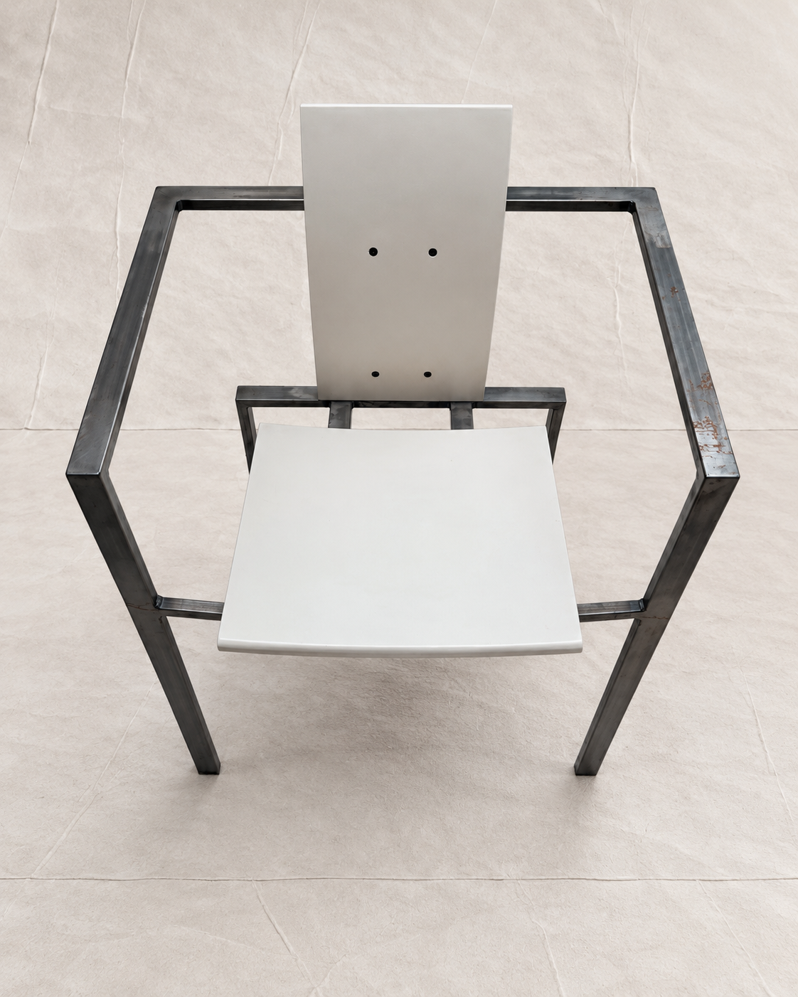 A modern minimalist chair with a white seat and backrest panel, supported by a black metal square frame, photographed from a top-down perspective on a light beige tiled floor.