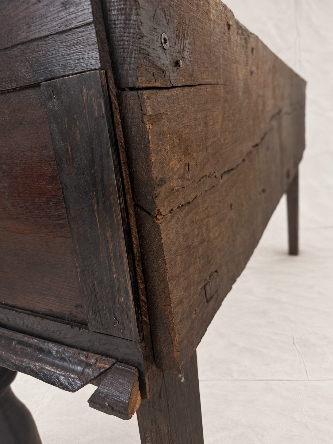 Close-up detail of a rustic dark wood table or bench showing the side panel, leg joint, and weathered plank construction on a light floor.