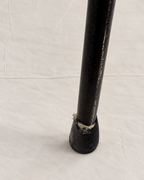 A close-up of a black metal table leg with a worn, chipped section near the base, set against a textured off-white background.