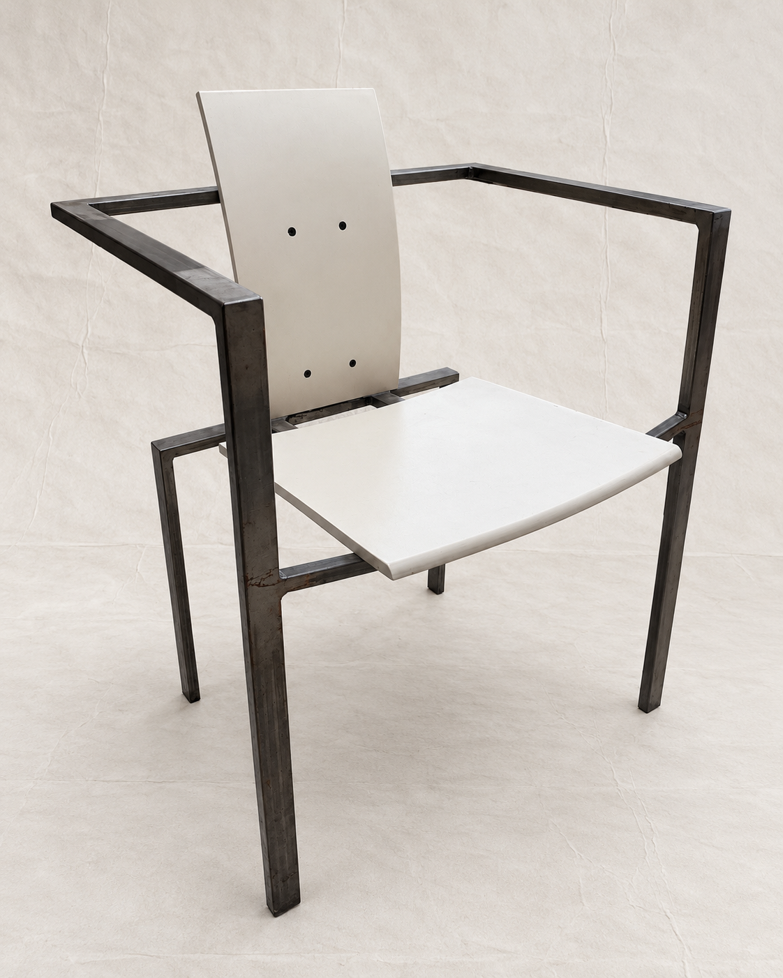 A modern armchair with a dark metal frame and light beige seat and back panels, photographed against a neutral light beige backdrop.