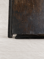 Close-up of the corner of a dark, distressed wooden cabinet or shelf with a black-painted frame, resting on a light gray fabric surface.