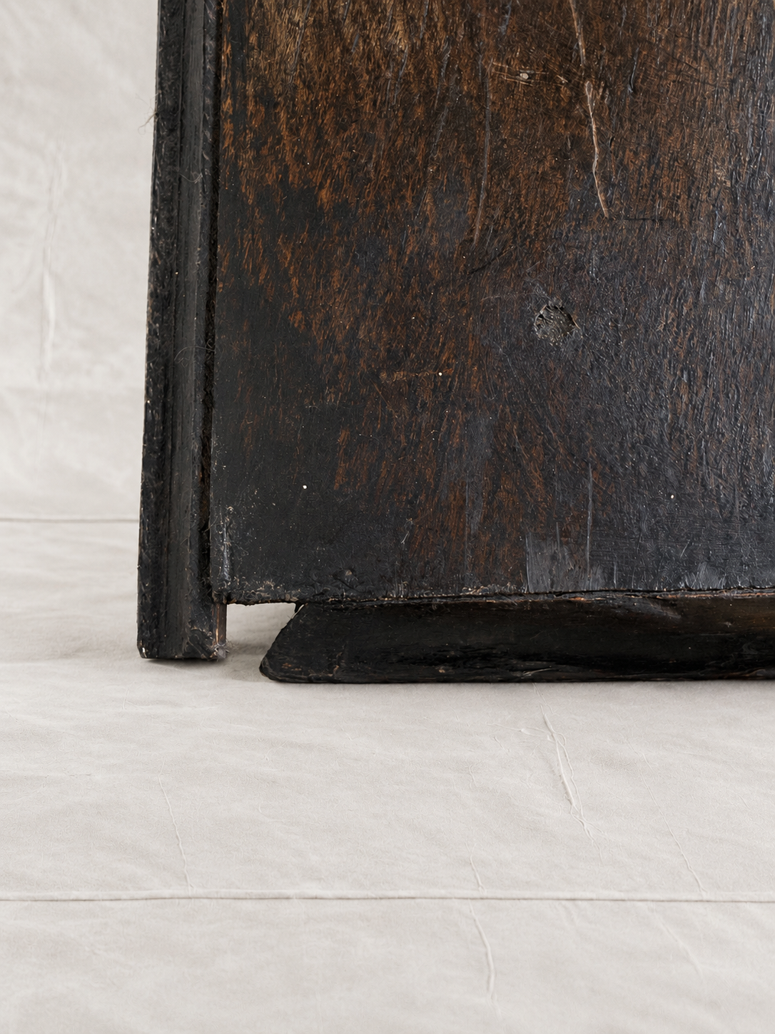 Close-up of the corner of a dark, distressed wooden cabinet or shelf with a black-painted frame, resting on a light gray fabric surface.