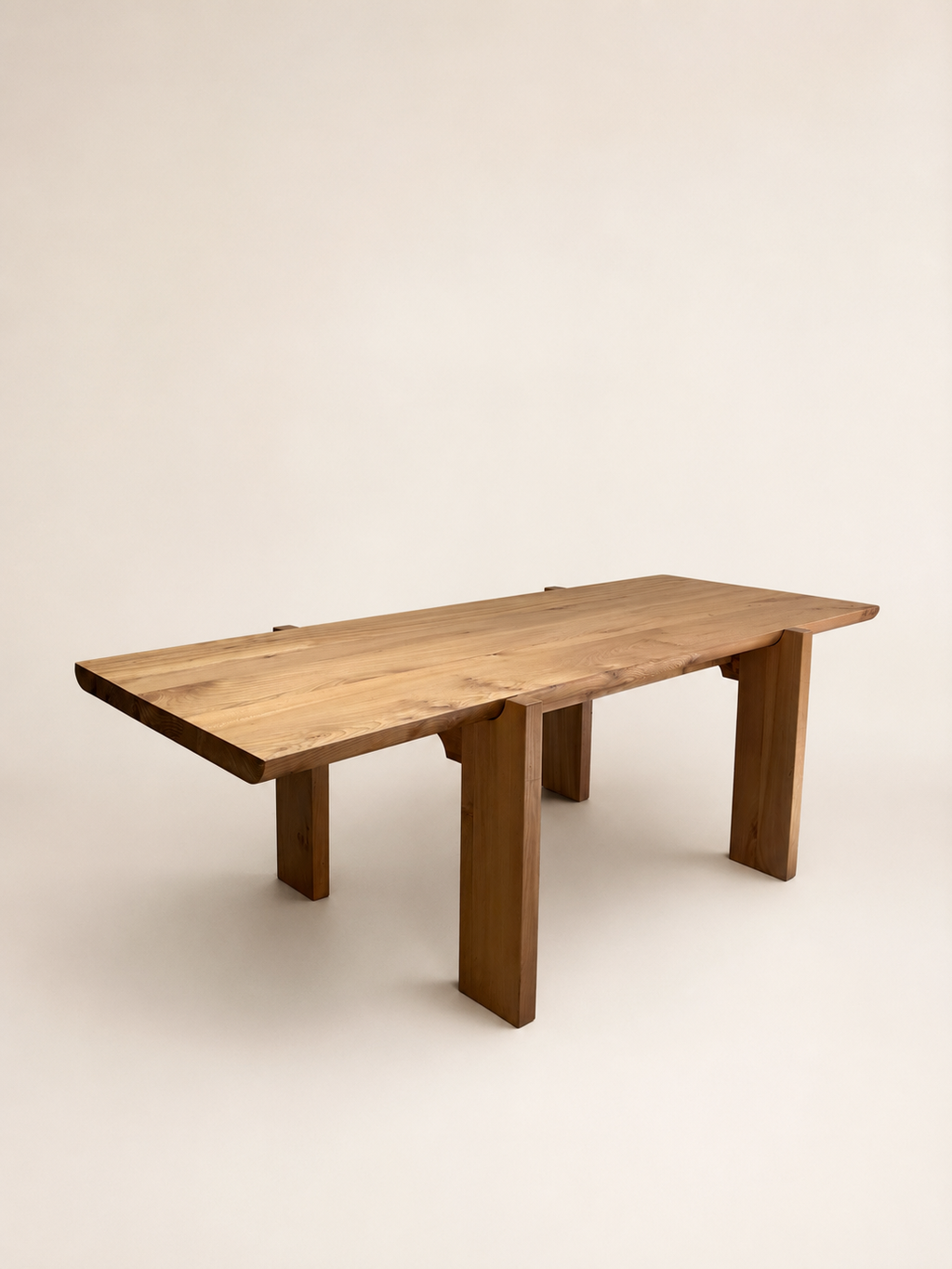 A rectangular wooden dining table with a live-edge top and thick block legs, shown on a plain warm off-white studio background.