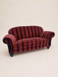 A vintage loveseat sofa with red and black striped velvet upholstery, featuring rolled arms, dark wooden legs, and small black caster wheels, photographed against a plain beige background.
