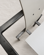 Close-up of a modern chair with a white upholstered seat and a dark charcoal metal frame, set against a neutral light beige fabric background.