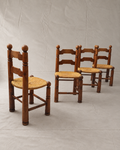 Four rustic Charles Dudouyt wooden dining chairs with woven straw seats, arranged on a light gray fabric backdrop.