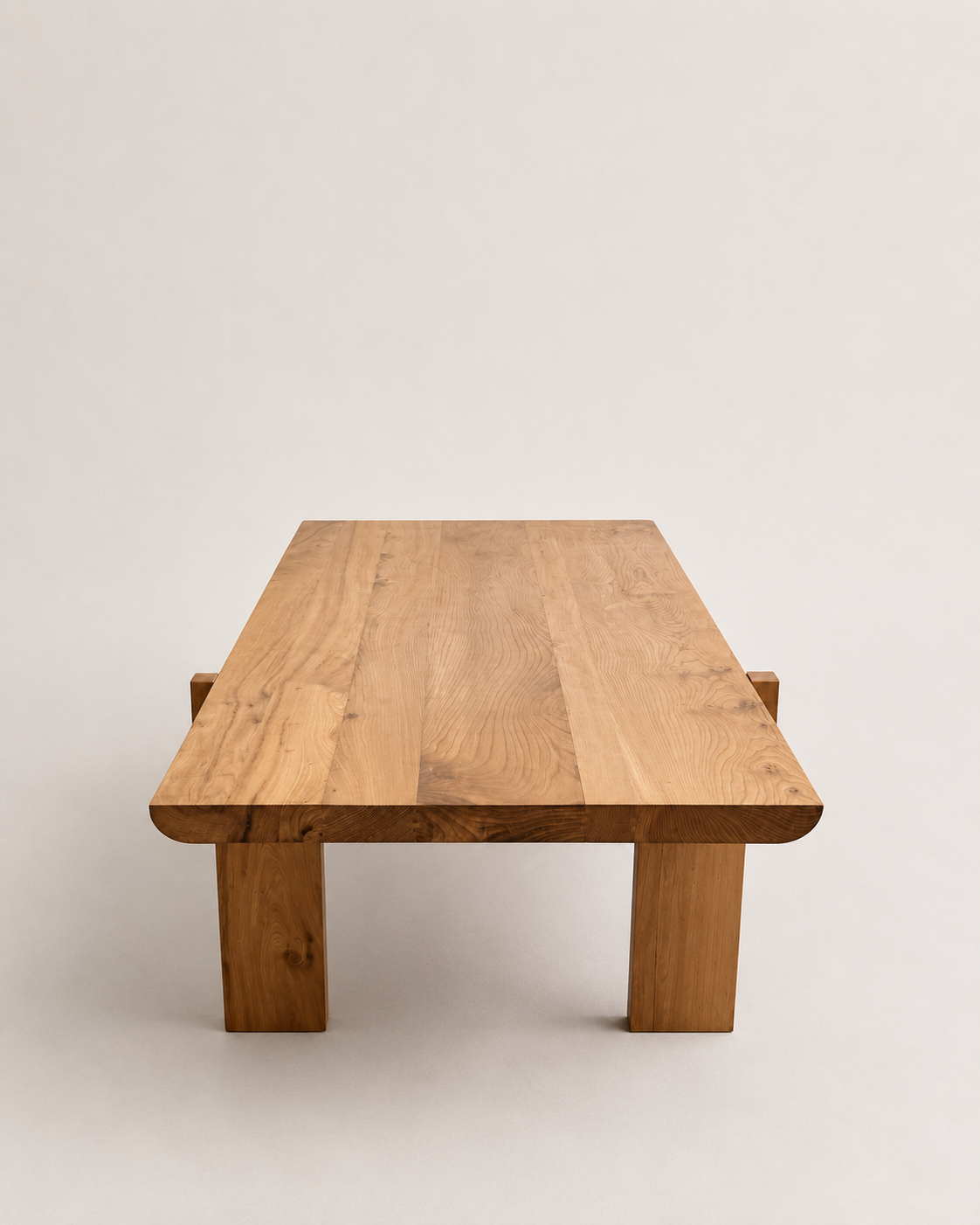 A minimalist rectangular wooden coffee table with a natural oak finish, featuring thick block legs and rounded corners, set against a plain light gray background.