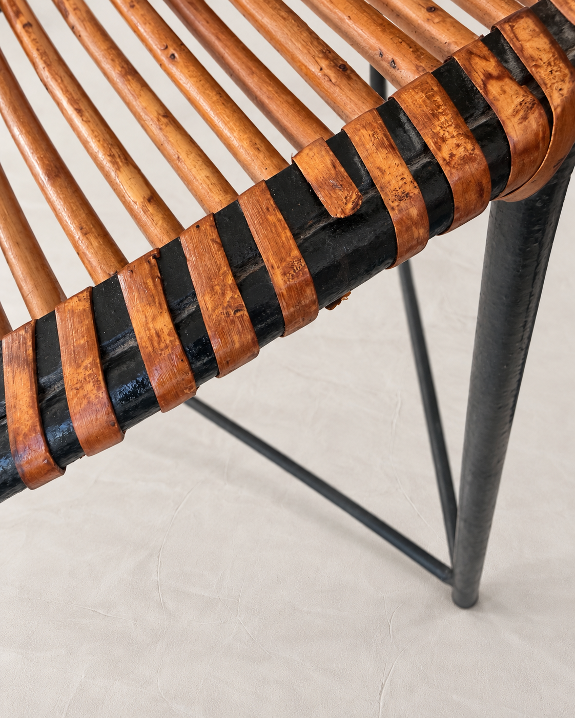 Close-up detail of a chair seat with curved brown leather straps wrapped around a black metal frame, set against a light beige textured floor.