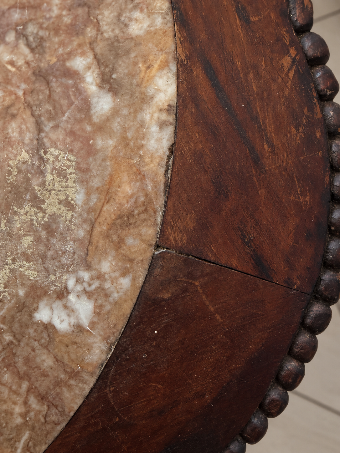 Close-up detail of a round table showing a dark brown wooden rim with a beaded edge and a warm beige and brown marble inlay.