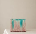 A rectangular ceramic vase with a textured, speckled glaze in pink and turquoise, sitting on a white draped table against a neutral beige background.