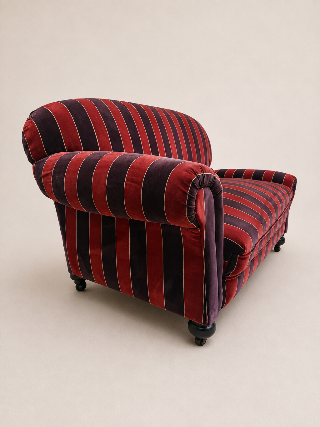 A vintage-style velvet armchair with bold vertical stripes in deep red and purple, shown from a three-quarters angle against a plain beige background.