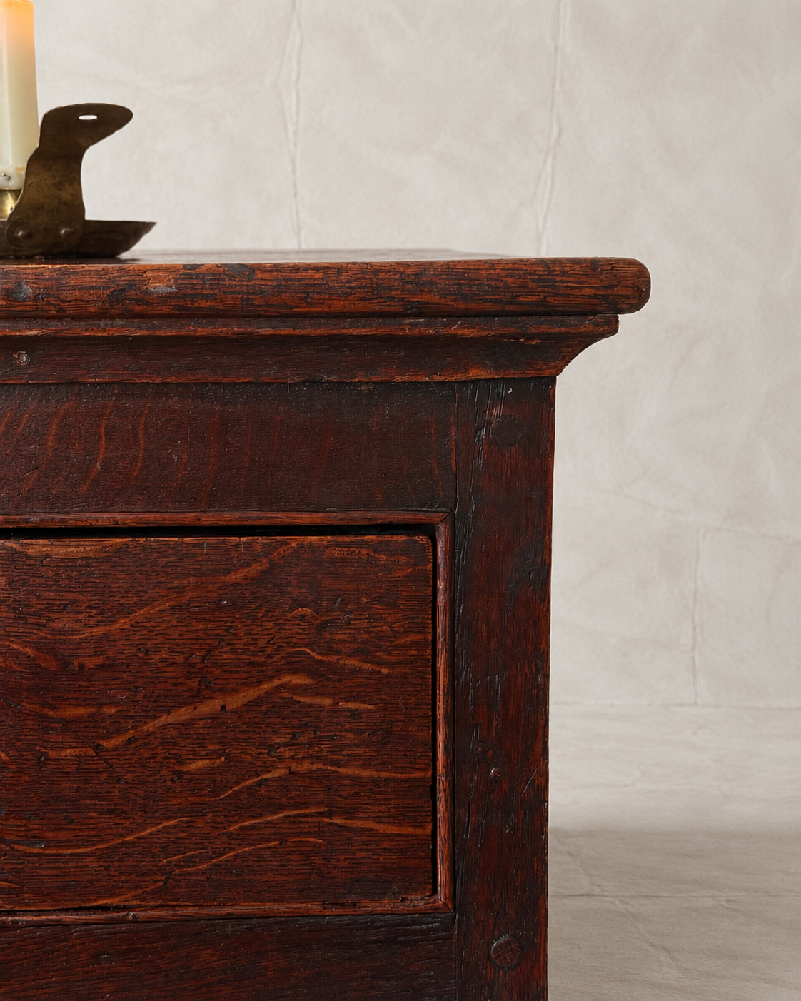 Close-up of a dark reddish-brown wooden chest or cabinet with a visible drawer front and natural wood grain, photographed against a light neutral wall.