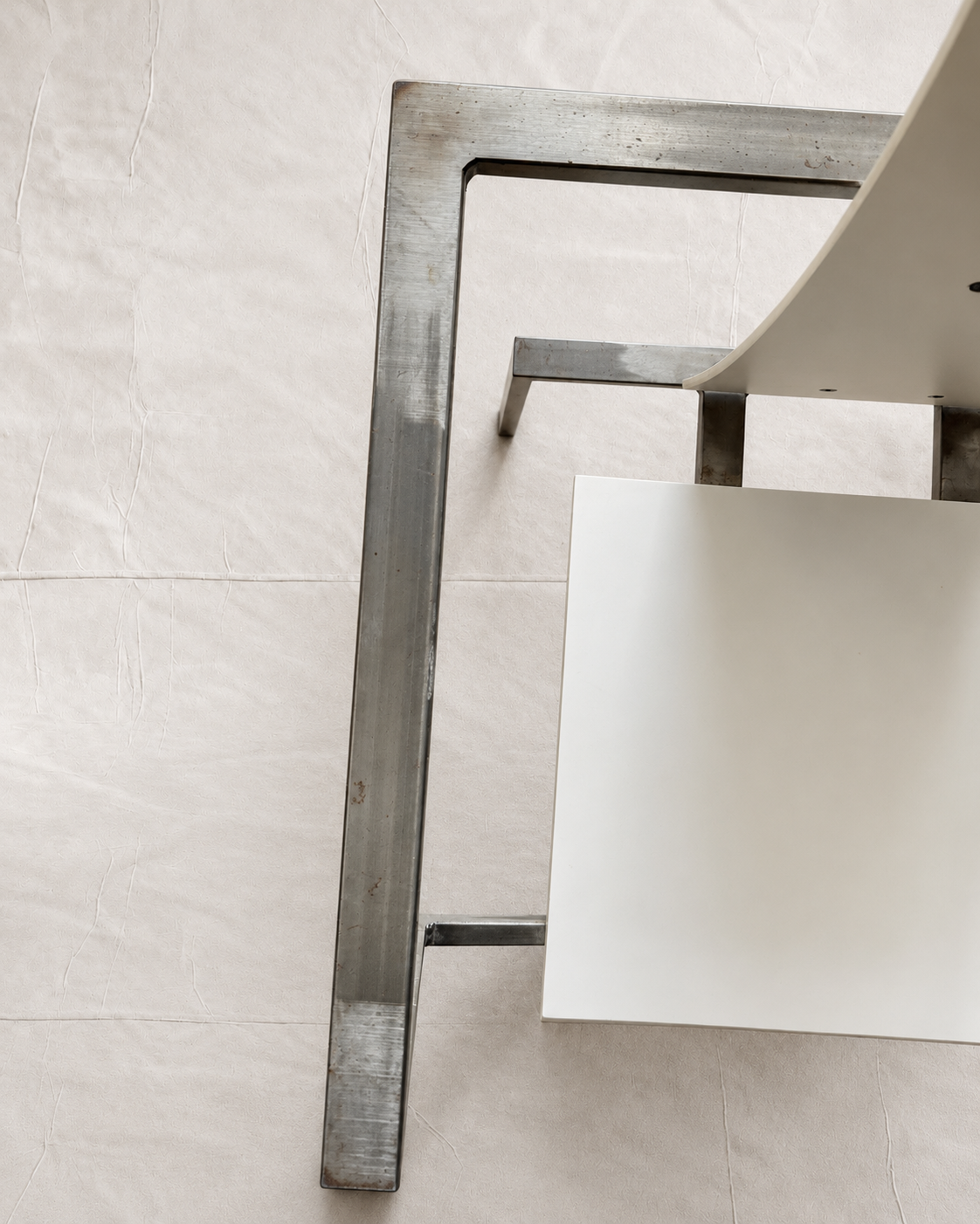 Close-up of a modern metal chair leg with a brushed silver finish, paired with a white seat and backrest, set against a light beige tiled floor.