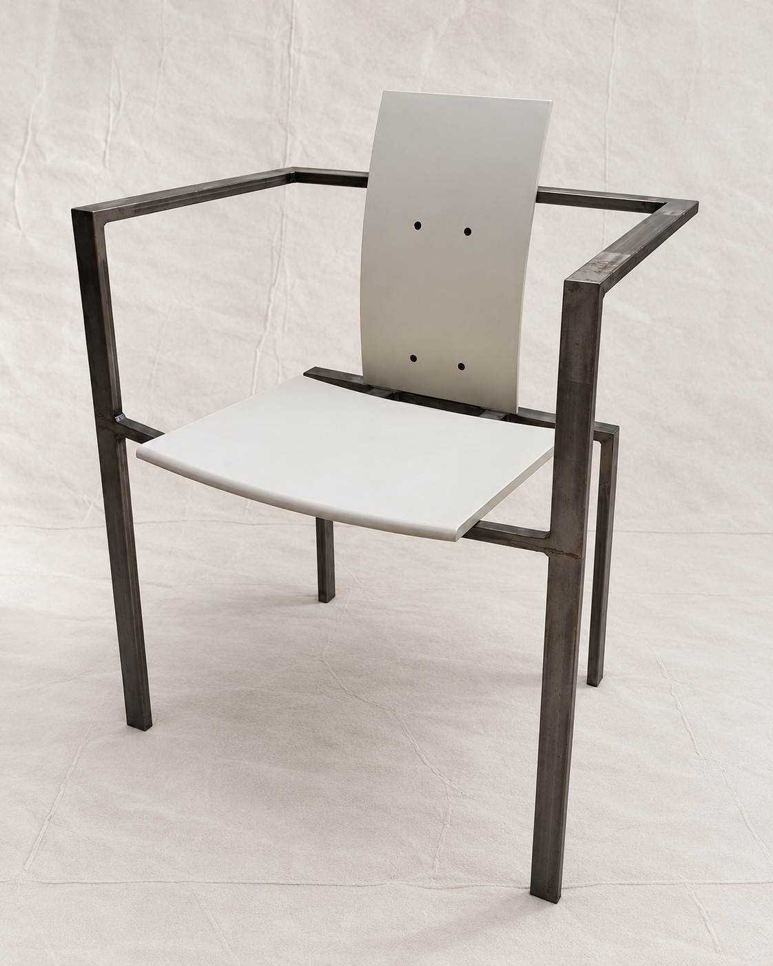 A modern industrial-style armchair with a dark metal frame and white seat and back panels, photographed against a light fabric backdrop.