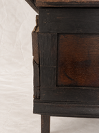 Close-up of a dark stained wooden furniture piece showing the side panel, front edge, and a visible crack in the wood, photographed against a white fabric backdrop.