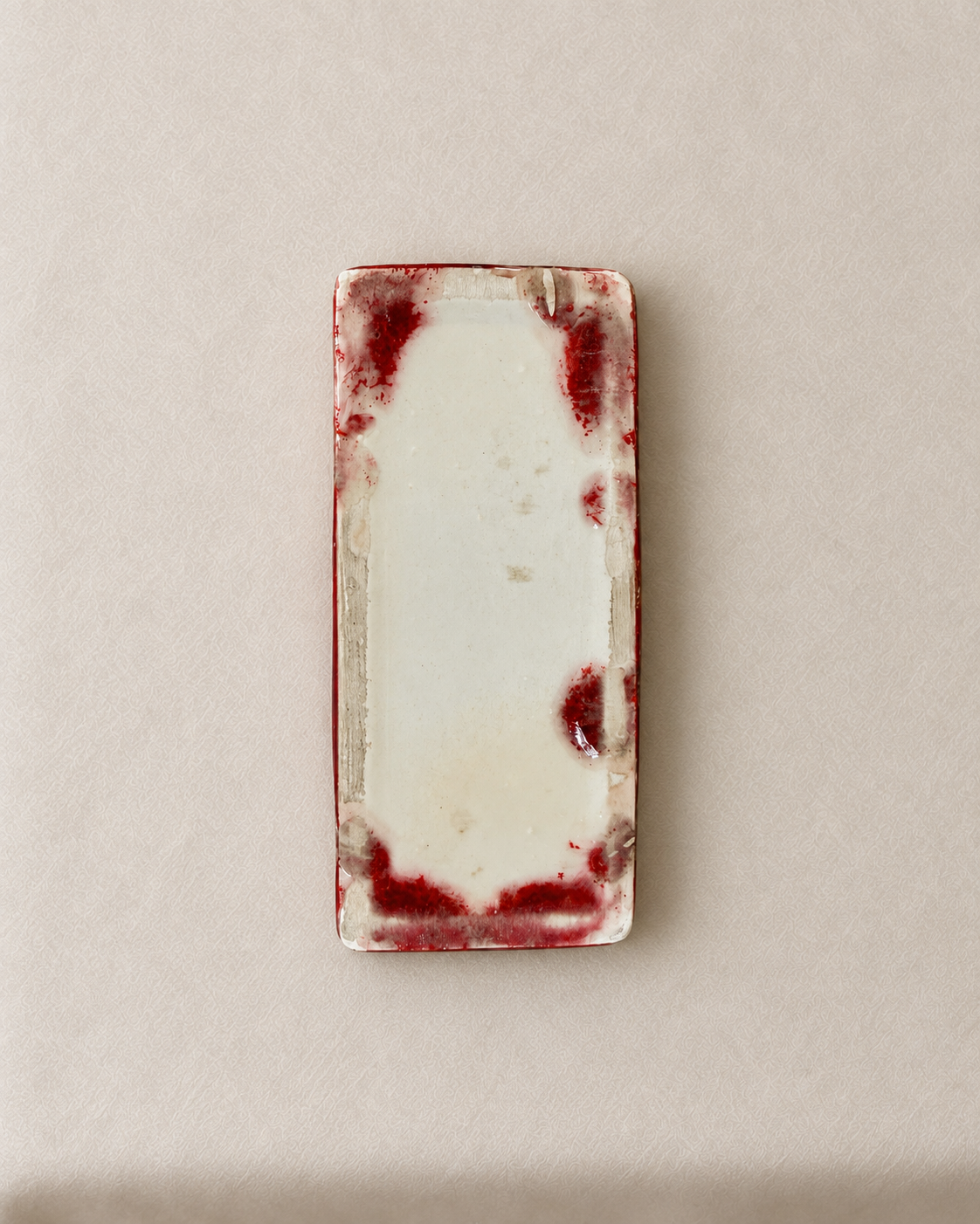 A rectangular ceramic vase with rounded corners, featuring a glossy off-white center and a textured, dark red glazed border with organic mottled patterns.