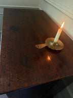 A lit white candle in an ornate brass holder resting on a dark wooden table.