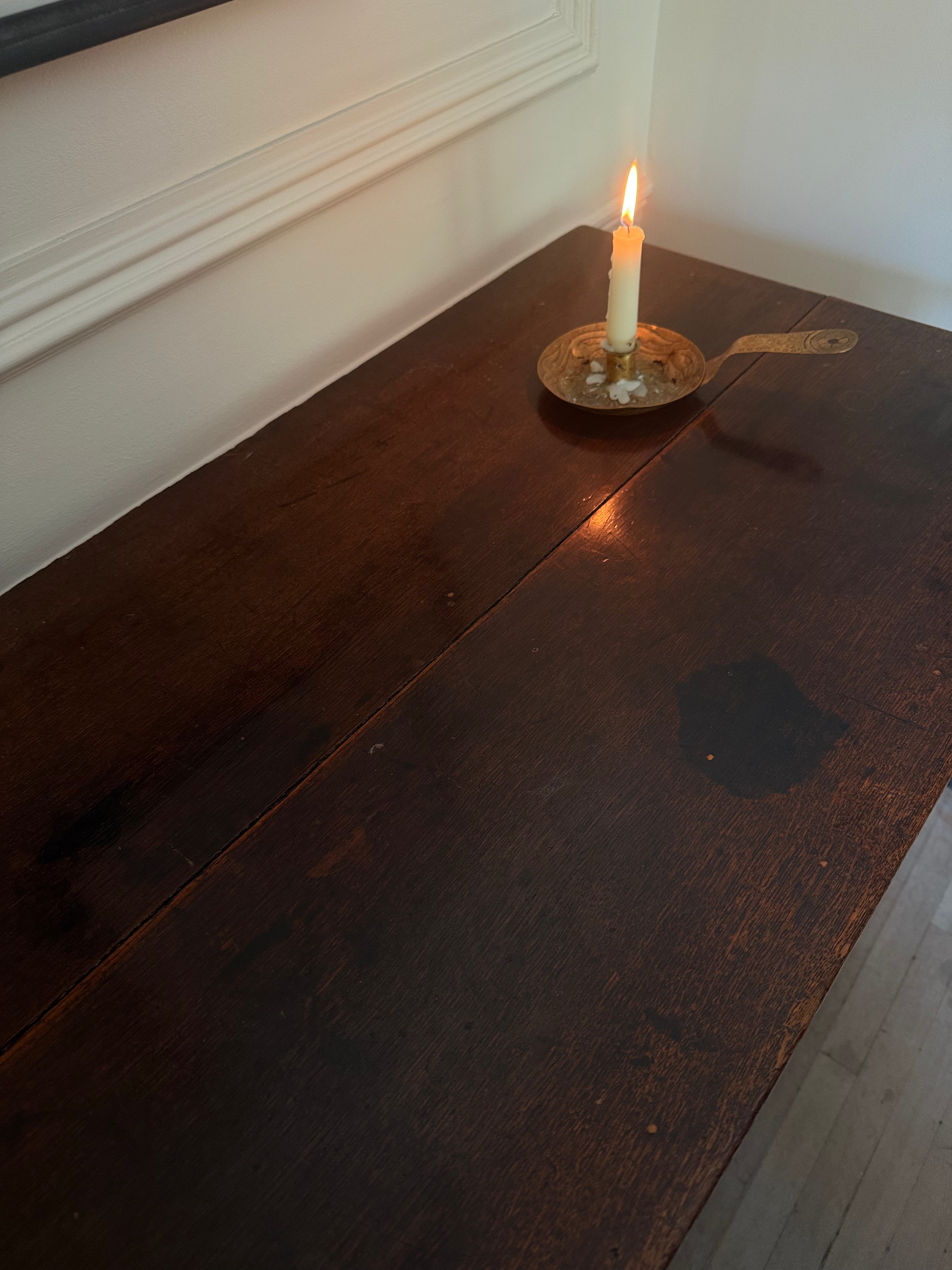 A dark brown wooden chest or table with a visible seam down the center, shown in a room setting with a lit white candle in a brass holder on top.