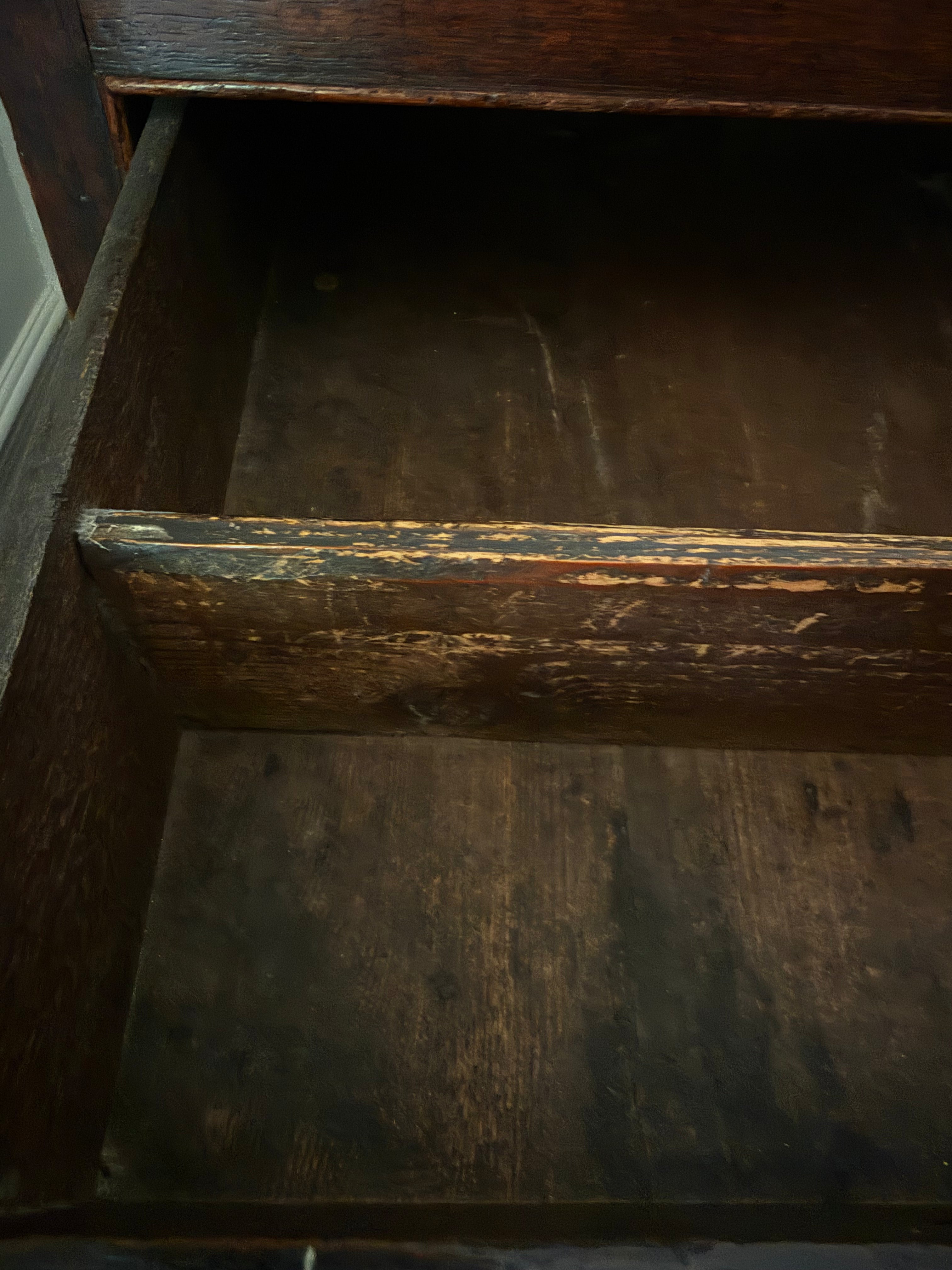 Close-up of the inside of a dark brown wooden drawer with a distressed finish showing worn wood grain and chipped paint.