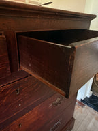 A close-up of a dark brown wooden dresser with one drawer pulled open, showing the interior. The photo is taken in a real room with visible floor and wall, so this is Lifestyle rather than Product/Packaging.