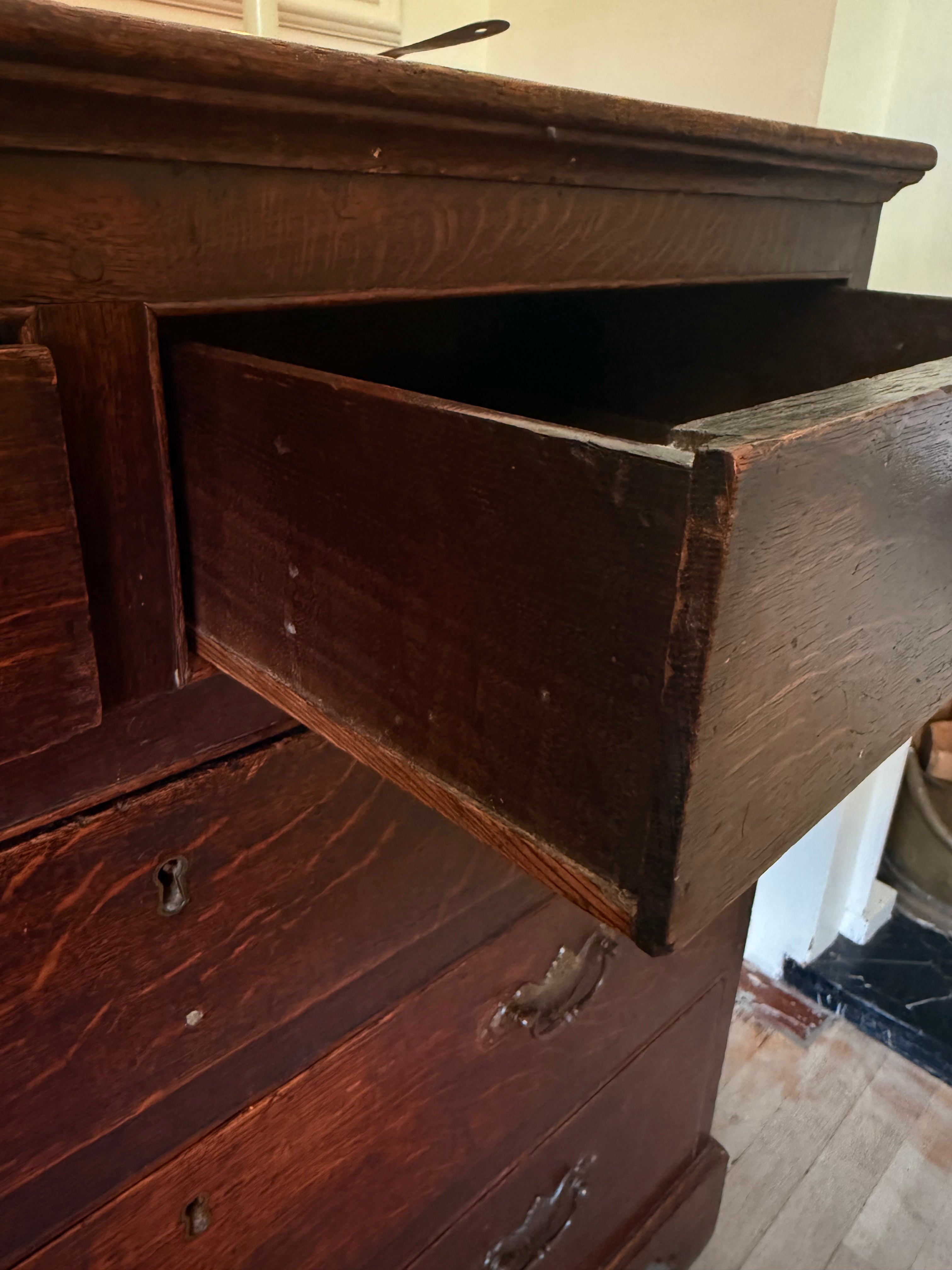 A close-up of a dark brown wooden dresser with one drawer pulled open, showing the interior. The photo is taken in a real room with visible floor and wall, so this is Lifestyle rather than Product/Packaging.