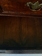 Close-up of the interior bottom panel of a dark brown wooden cabinet or chest, showing wood grain, a brass pull handle at the top, and a dark frame edge.